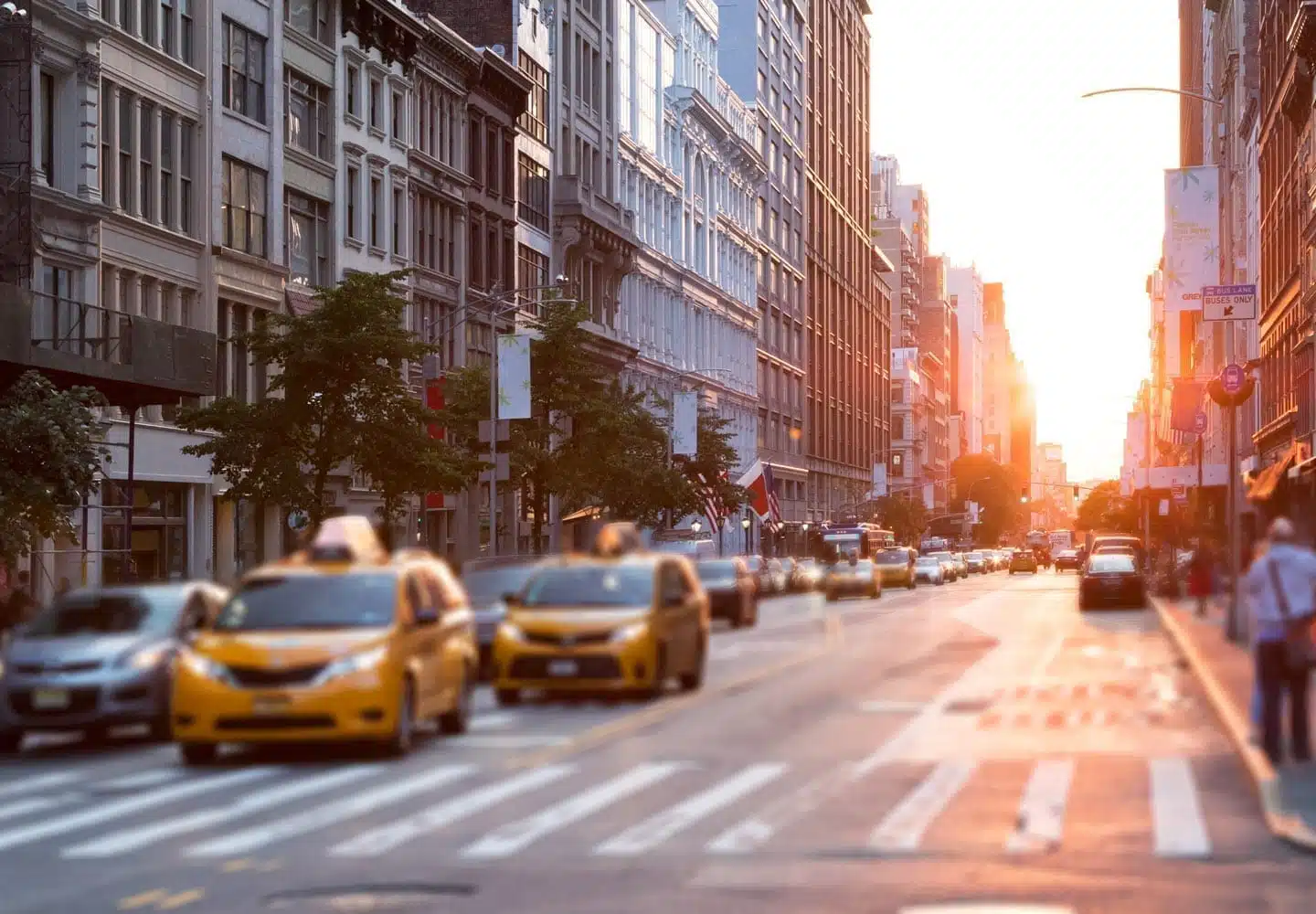 Yellow cabs are driving down a busy street in Manhattan during sunset.