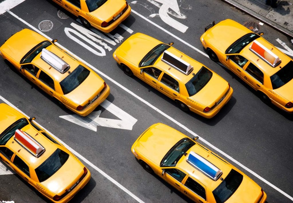 An aerial view of six yellow taxi cabs dispersed across four lanes of traffic in New York City.