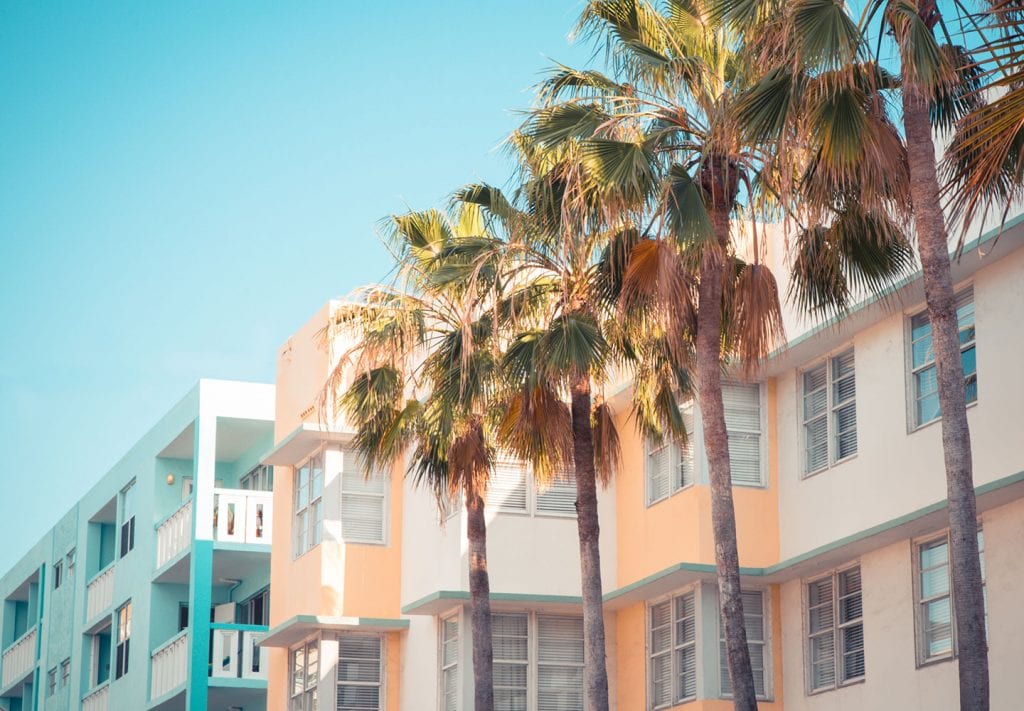 Palm trees beside colorful Miami apartment buildings, set against a clear, blue sky.