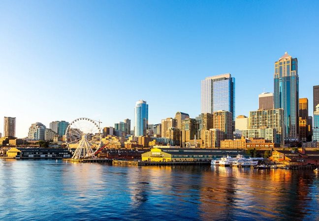A distant view of Pike Place Market, the Seattle Great Wheel, and the surrounding skyscrapers from the waterfront in Downtown Seattle.