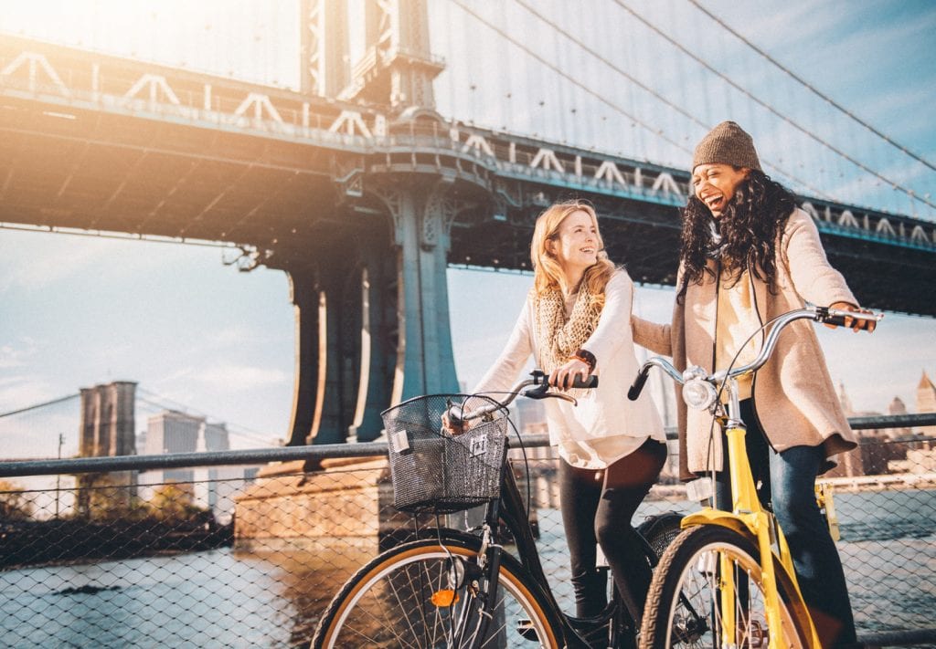 Two women on bikes, taking a break under the Brooklyn Bridge.