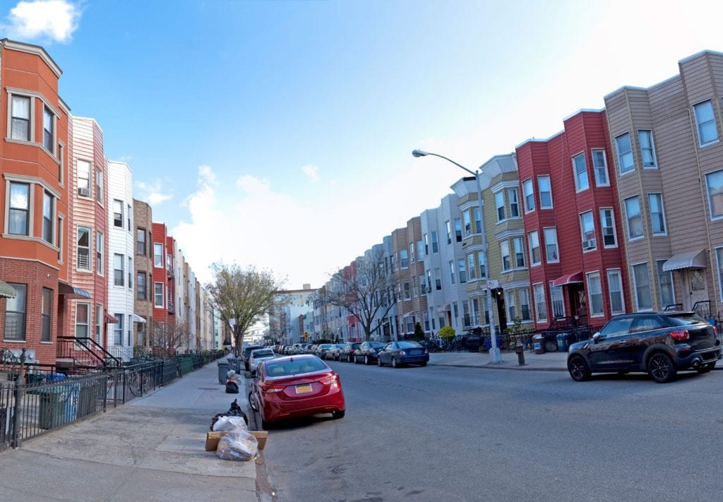 A residential street in the Brooklyn Neighborhood Greenpoint, with similar apartment buildings lining each side of the street.
