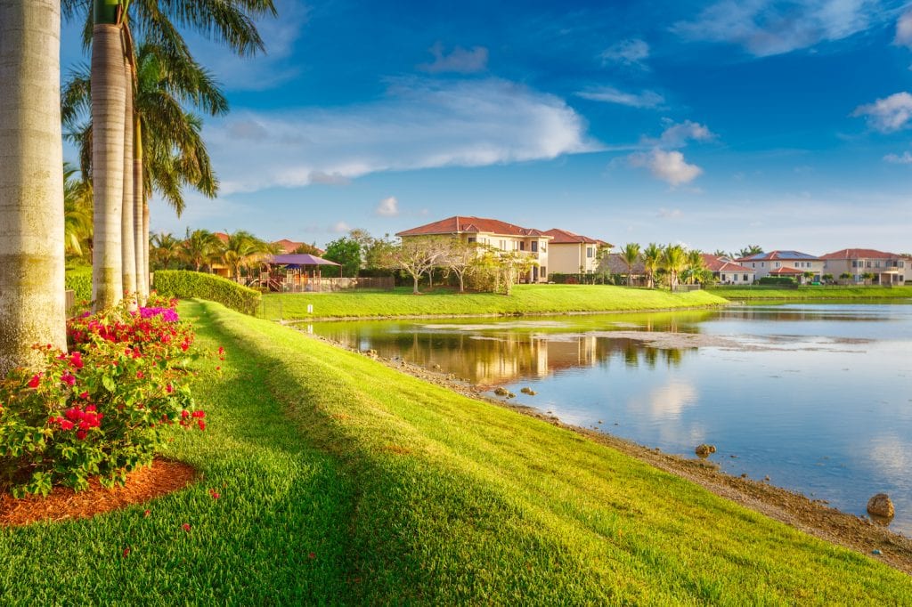 Lines of homes on a pond in a residential neighborhood in Miami. There are palm trees and flower beds. 