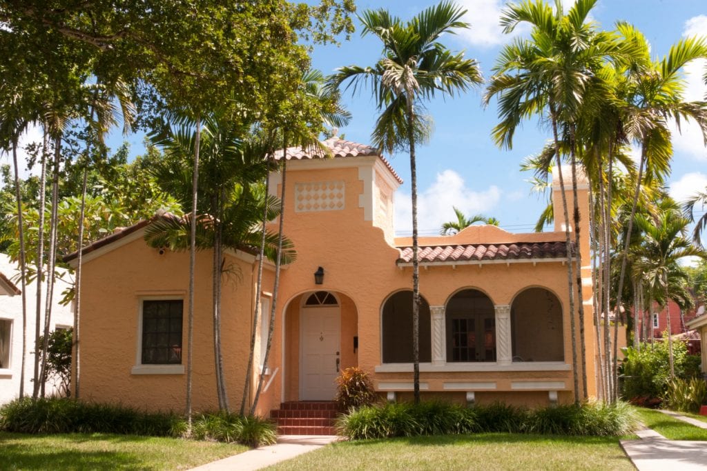 An organge one-story home in Miami, Florida. The front yard has palm trees and green grass. 