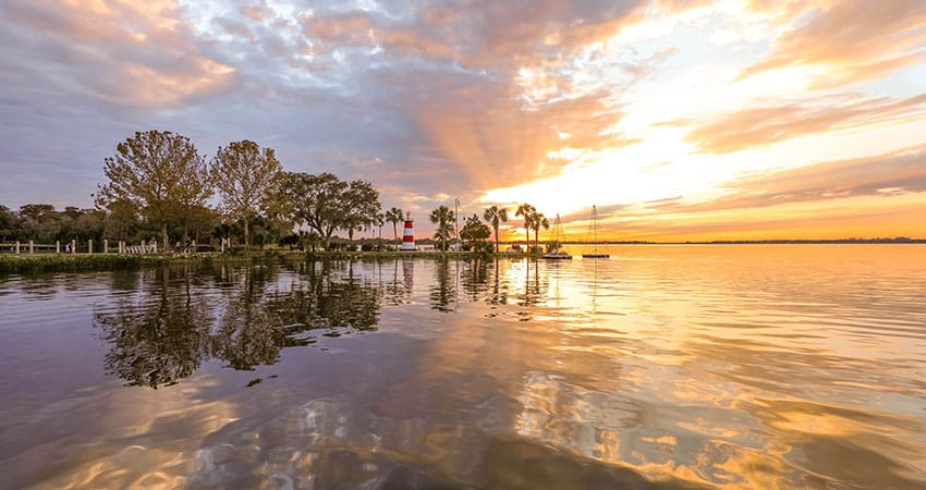 The sun shines over Lake Dora, painting the sky in rich oranges and yellow. Mount Dora's lighthouse stands over the water. 