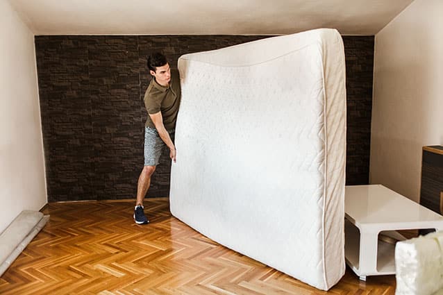 A man moves his mattress into his new bedroom. He is holding the mattress on its to make it easier to move.  