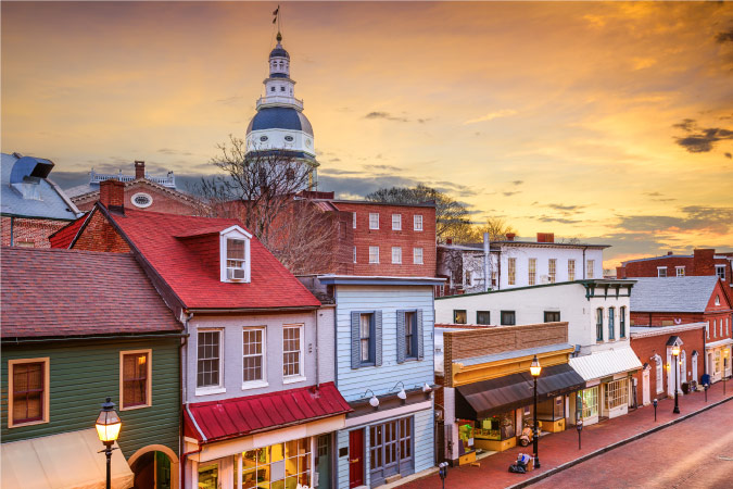 A variety of historic buildings in Downtown Annapolis, Maryland, seem to shine in the faint remaining light before the sun sets. Behind this row of shops, the State House is jutting up far above the rest of the buildings.  