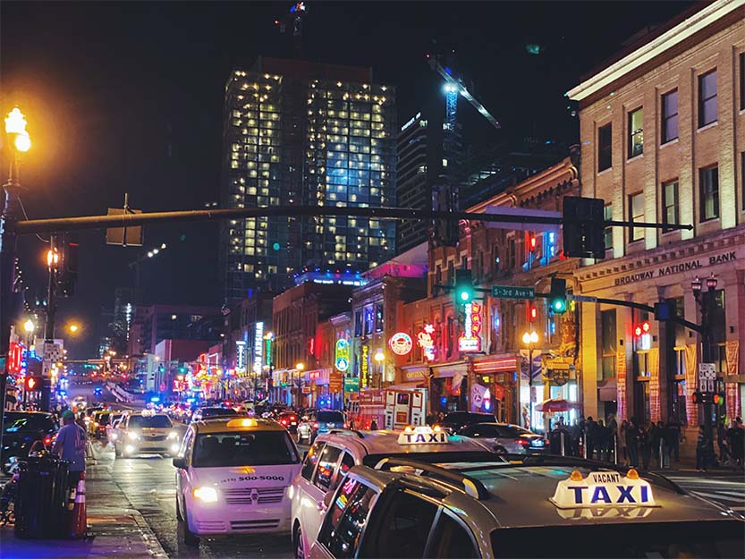 Private cars and taxi cabs navigate traffic through The District in Nashville.