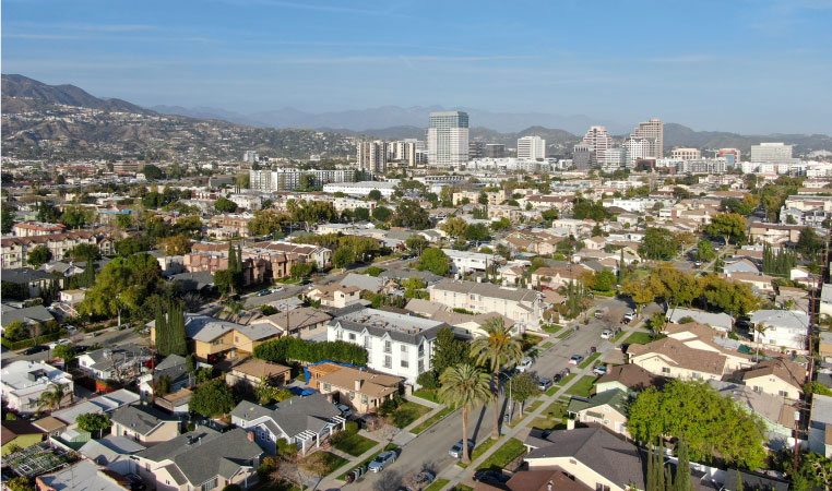 Aerial view of downtown Glendale, California, with rows of residential buildings in the foreground and mountains in the background. 