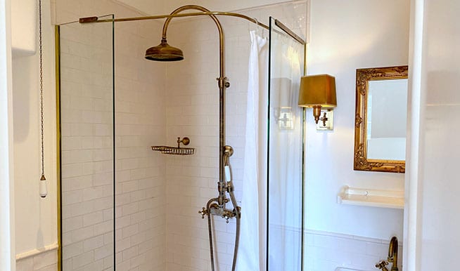 A shower with glass doors. The shower head and nozzles are old-school brass