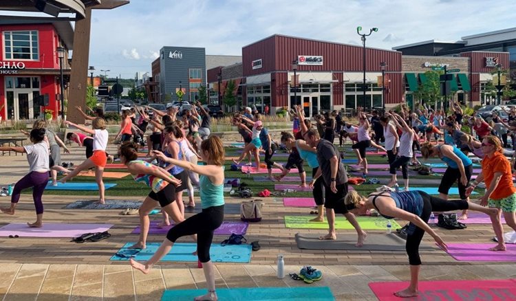 The King of Prussia Town Center, hosting an outdoor yoga event for the community. Dozens of locals are standing on colorful yoga mats as they follow along.