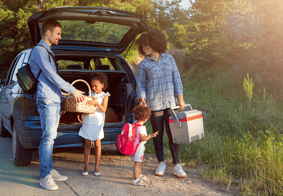 A young family unloads their car for a picnic in the grass