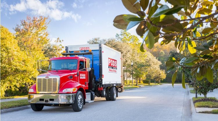 A PODS truck is transporting a PODS portable moving container through a residential neighborhood in one of the best small towns in South Carolina.
