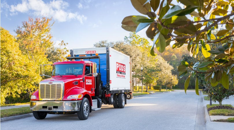 A PODS truck is transporting a PODS portable moving container on a sunny day.