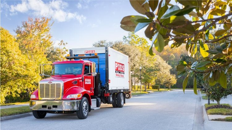 A PODS truck transporting a portable moving and storage container through a neighborhood in a small town in North Carolina.