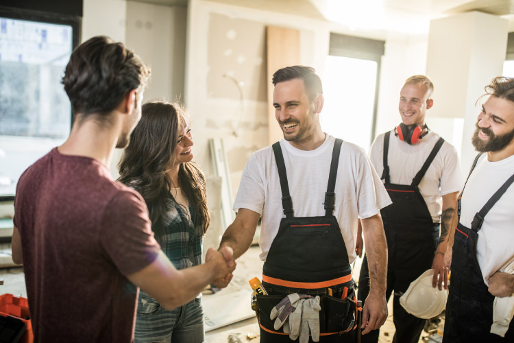 A team of three friendly construction workers meets with the homeowners in a partially remodeled room.