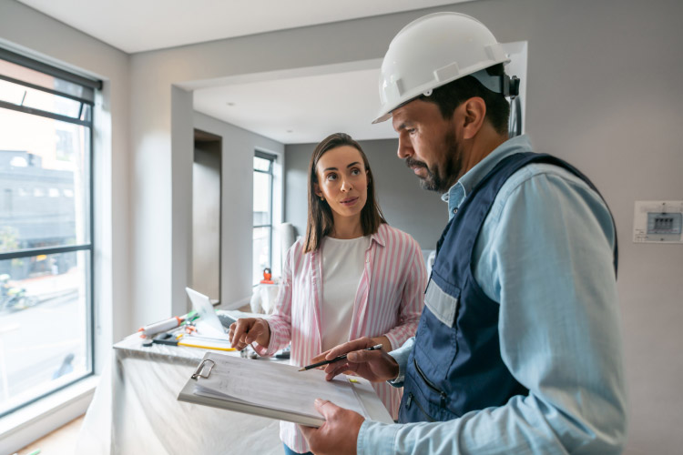 A woman is asking her remodeling contractor questions as he looks over paperwork on a clipboard.