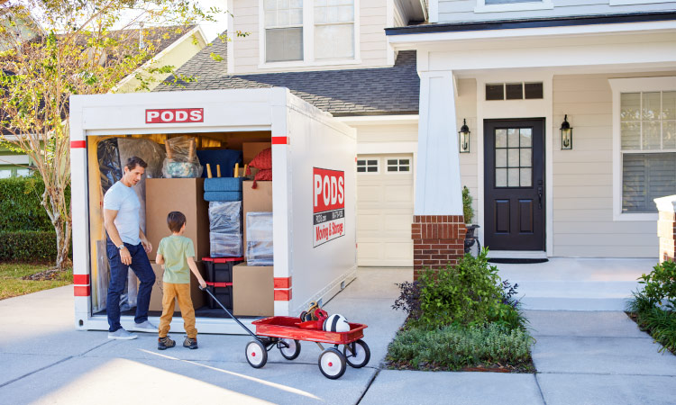 A father and son are standing in their driveway at the entrance of a fully loaded PODS storage container, which was selected based on the info in our storage unit size guide.