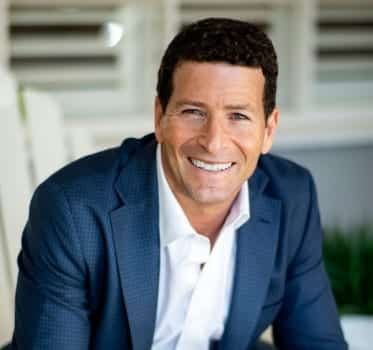 The headshot of Dan Urbach, Malibu real estate agent. He is in a blue suit jacket and is smiling. 