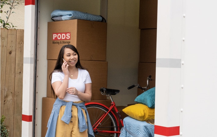 A woman standing beside a loaded PODS portable moving container, talking on her cell phone.