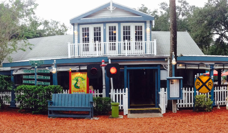 Molly Goodheads Raw Bar & Restaurant in Palm Harbor, FL. A blue two-story building welcomes customers in with a bright yellow sign featuring a flirty mermaid.
