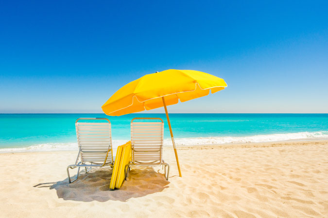 View from behind of a pair of empty beach chairs and a yellow umbrella on South Beach in Miami, Florida.