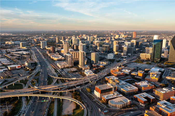 Aerial view of Downtown Dallas, featuring city skyscrapers and a complex network of freeways with overpasses.