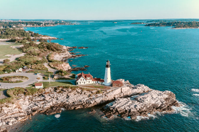 Aerial view of Portland Head Light outside of Portland, Maine, featuring rocky cliffs and deep blue waters.