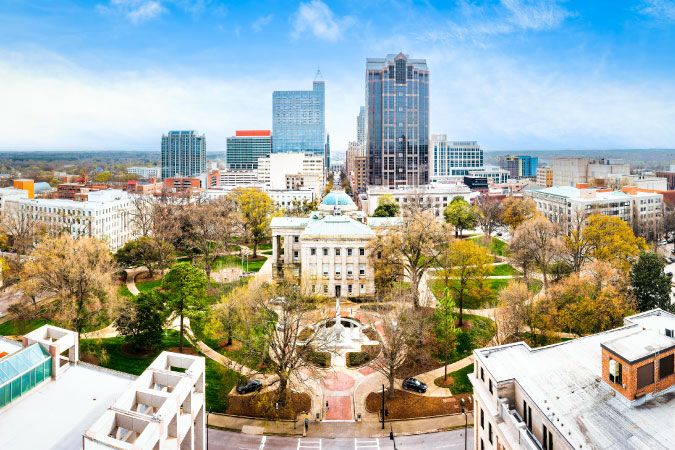 Aerial view of the North Carolina State Capitol and Raleigh city skyline on a clear, sunny day.