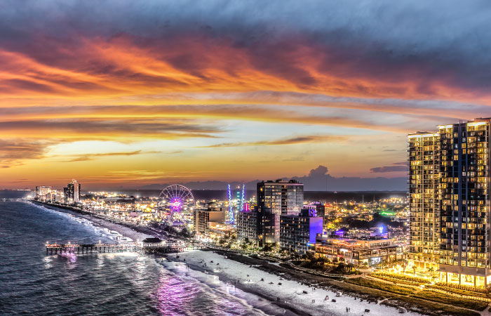 Evening view of Myrtle Beach, South Carolina, with all the buildings and attractions illuminated against a sunset sky.