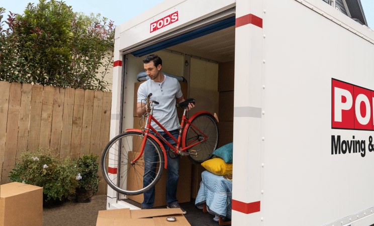 A man is unloading a bike from a PODS portable moving container after  moving to Portland, Oregon.