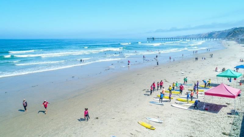 A group of people are gathered beside an array of surfboards as they partake in the Surf Diva Surf School on La Jolla Beach outside San Diego. 