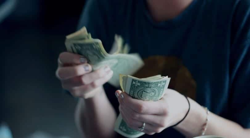 A close-up view of a young woman's hands counting cash by moving it from one hand to the other.