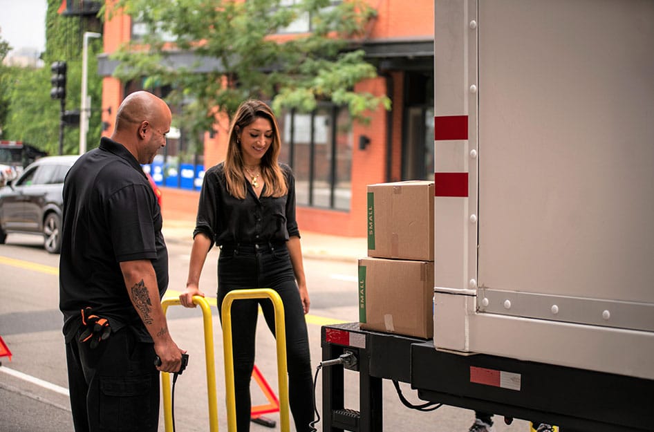 A young woman is smiling as she speaks with a PODS driver beside her PODS moving container. She is using PODS City Service to move into her NYC apartment.