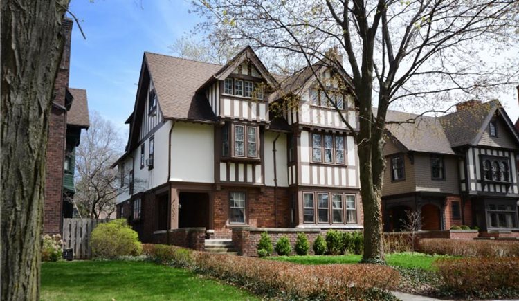 A pair of lovely Tudor-style homes in Detroit’s historic Indian Village neighborhood. The yards are lined with low bushes, and there’s a single tree in the yard of the closest home.