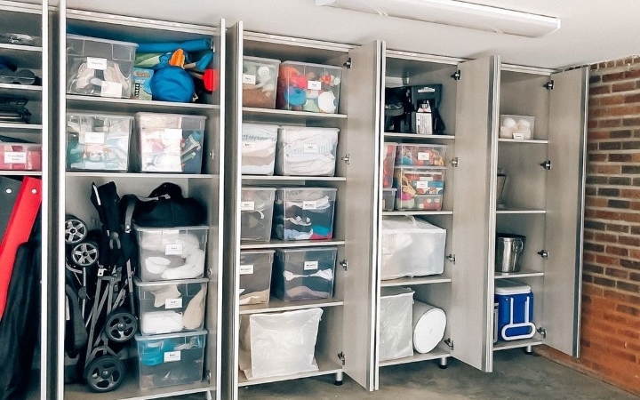 A garage wall that has been organized with side-by-side, floor-to-ceiling cabinets. The doors of the cabinets are open, revealing shelves that are neatly organized with clear plastic bins and other items. 