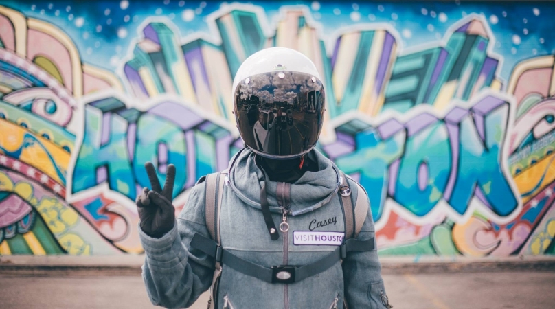 A person wearing motorcycle gear poses for a picture in front of a colorful mural in Houston, Texas.