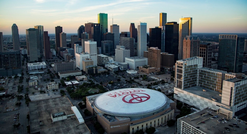 An aerial view of Houston, Texas, with the Toyota Center in the foreground and tall city skyscrapers in the background.