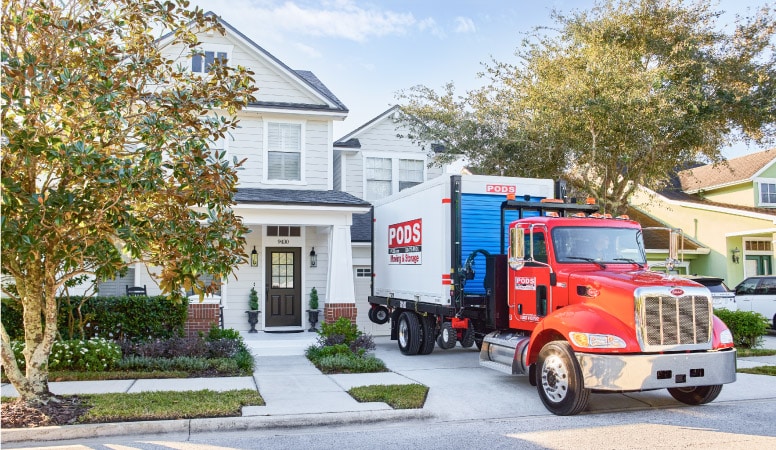 A PODS truck with a PODS moving and storage container on the back is reversed into a residential driveway. The driver is about to use PODZILLA to place the container in the driveway.  