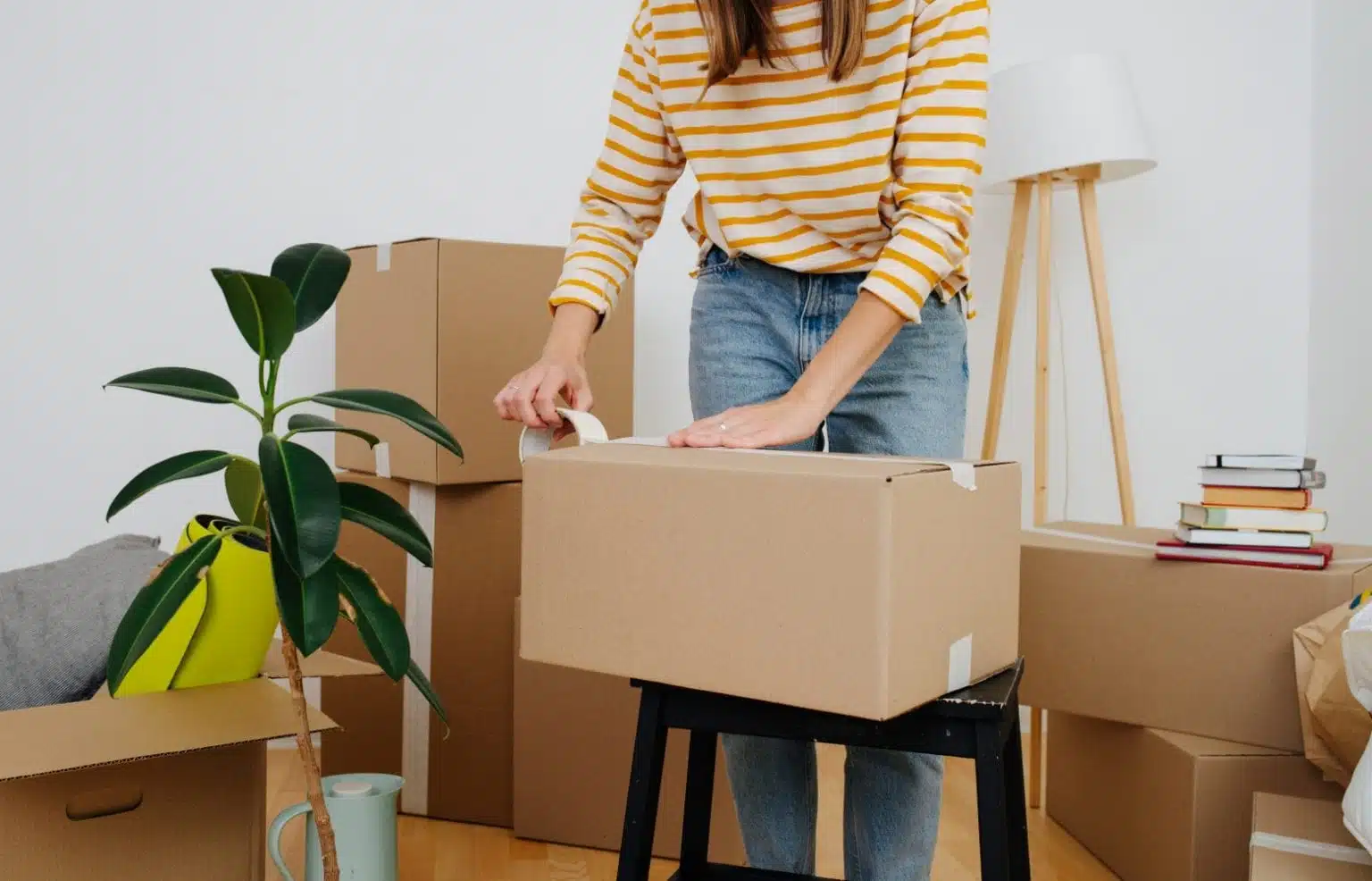 A woman in a yellow striped top tapes up a cardboard box