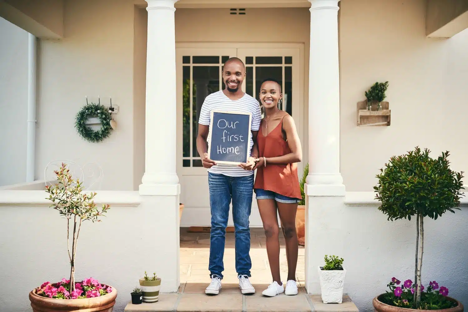 couple outside first home holding sign