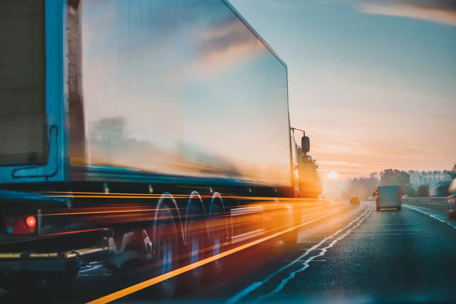 A moving truck drives down a highway with the sunrise in the foreground.
