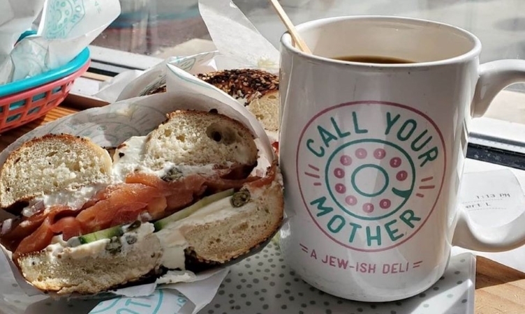 A close-up view of a lox and cucumber bagel sandwich and a cup of fresh coffee from Call Your Mother Deli in Washington, D.C.