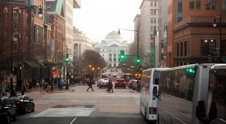 A foggy view of pedestrians crossing a busy street in Washington, D.C., with cars and public transportation all around.