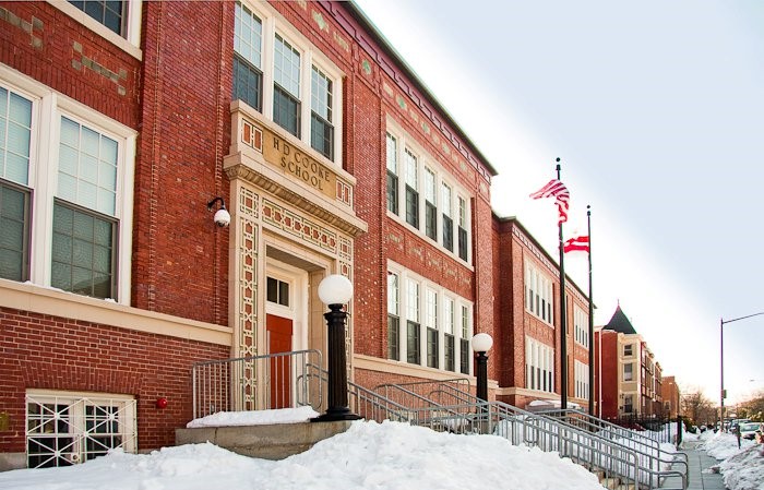 An angled view of H.D. Cooke Elementary School in Washington, D.C., after a snowstorm. The red brick of the buildings seems brighter than usual against the white snow banks that abut the building and its entrances.