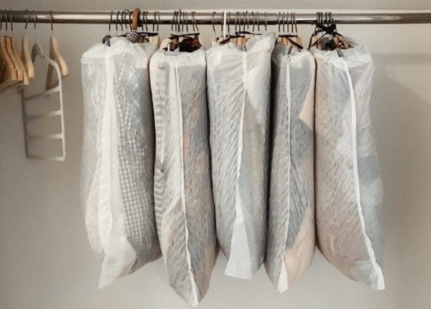 Five bunches of clothes are hung up in a closet. They’re protected by white garbage bags, which will keep them from getting dirty and also make them easy to transport during a move.