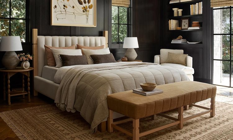 A brown frame bed sits in the center of the room with three rows of brown pillows. There are two nightstands with lamps on either side and decorations throughout.  