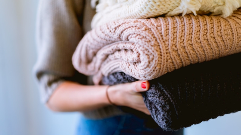 Close-up view of a woman holding a pile of extra blankets for her Airbnb guests.
