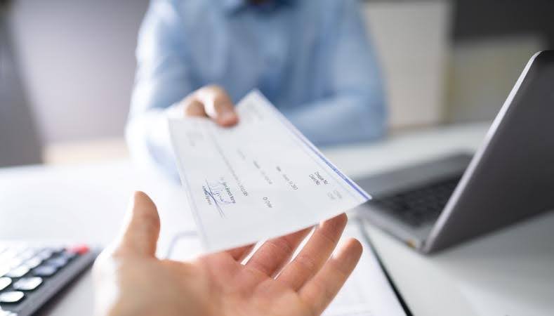 A man is reaching across his desk with a check — a lump sum payment that is part of a new employee’s job relocation package.