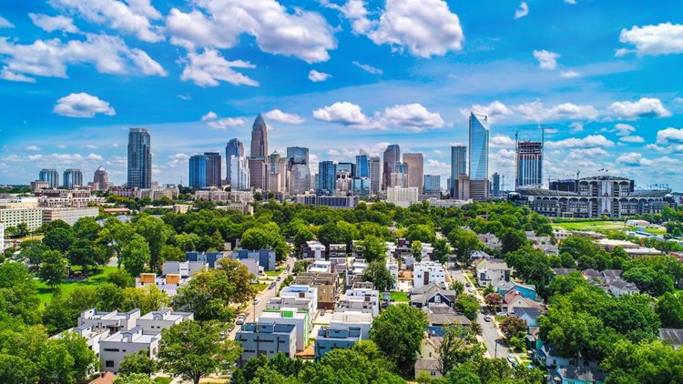 A bird’s-eye view of Uptown Charlotte on a bright, summer day. Tall buildings fill the skyline in the distance and shorter, residential buildings and lush trees fill the foreground.